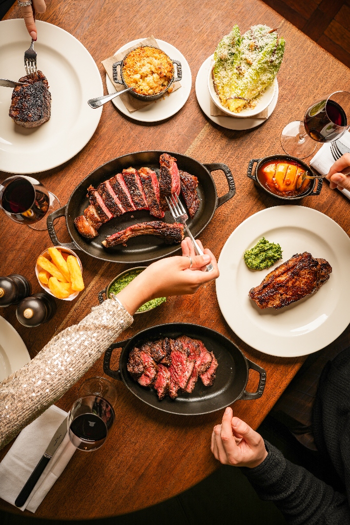 Food on a table shown from above with the focus on steak being served.